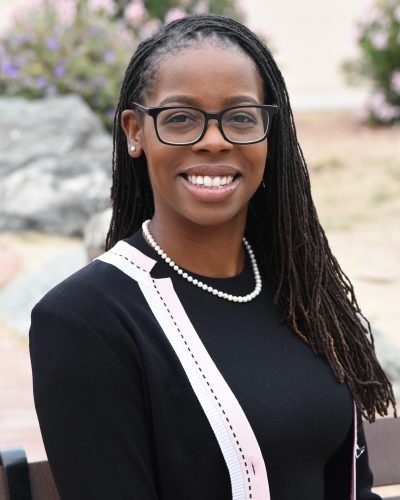 Professional headshot by Laura Voight: smiling woman with braids, glasses, and a pearl necklace
