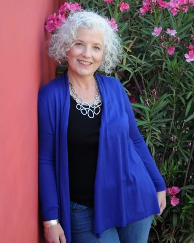 Outdoor portrait by Laura Voight: woman with white curly hair in a blue cardigan beside a pink wall